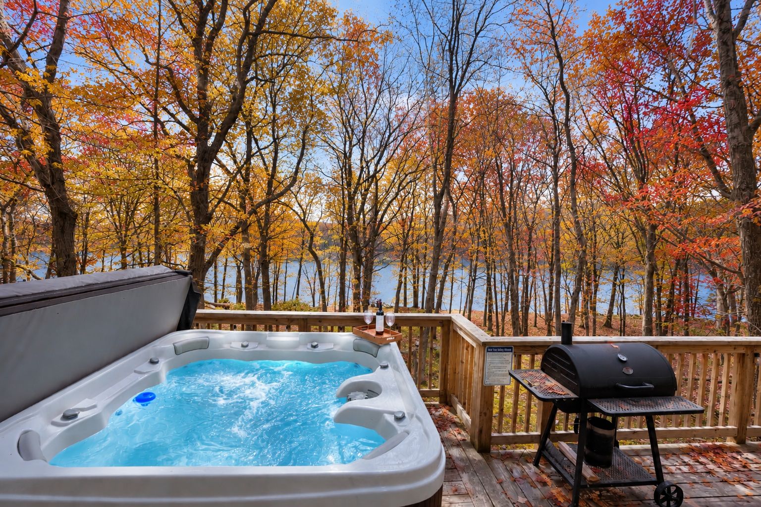 A hot tub on a deck with a view of a lake and autumn trees.