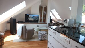 A modern kitchen with a large TV, white cabinets, a glass coffee table, and a dining area with a chair. - Ferienwohnungen Ries (Eusserthal)