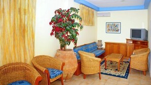 Una sala de estar con muebles de mimbre, una planta grande, un televisor y un cuadro en la pared.