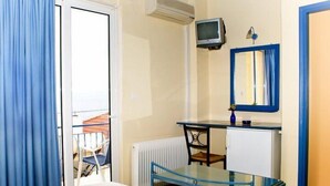 Una habitación de hotel con una cama, un escritorio con computadora, un radiador pequeño y una ventana con cortinas.