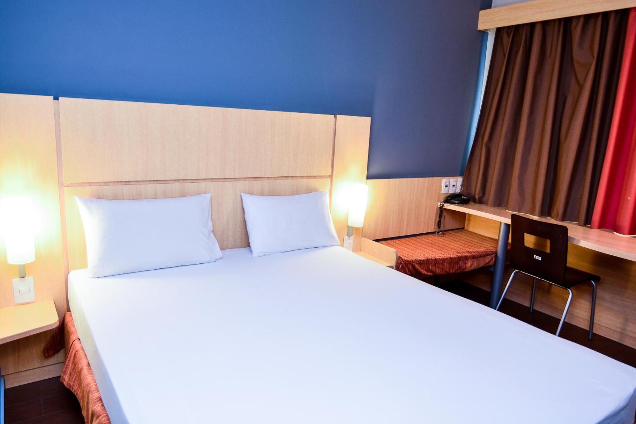 Habitació d'hotel amb un llit gran, dues làmpades de nit, un escriptori amb una cadira i una cortina.