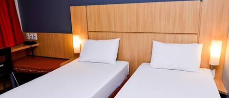 Una habitación de hotel con dos camas individuales, cabeceros de madera y lámparas de noche.