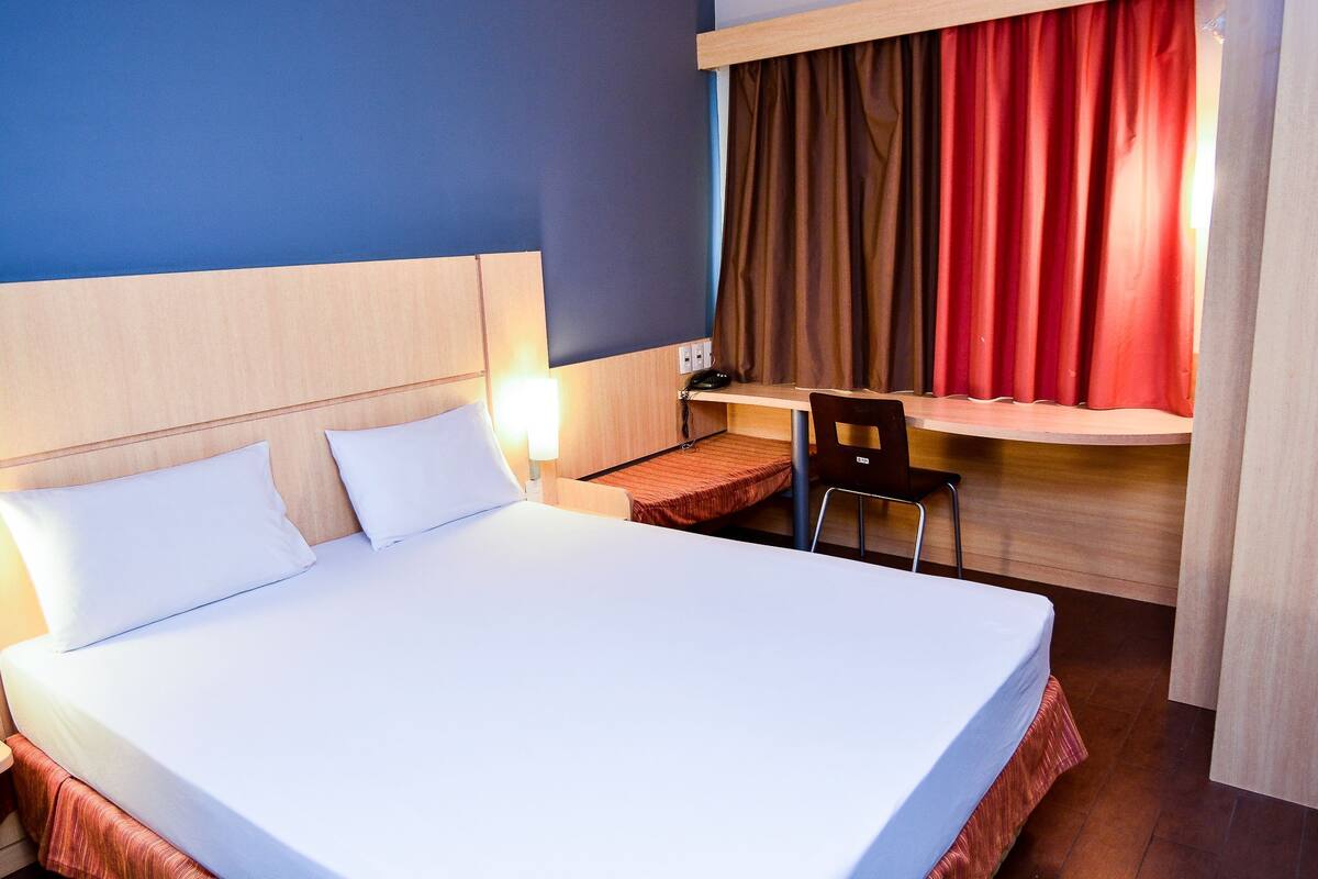 A hotel room with a bed, a desk, a chair, and a curtain.