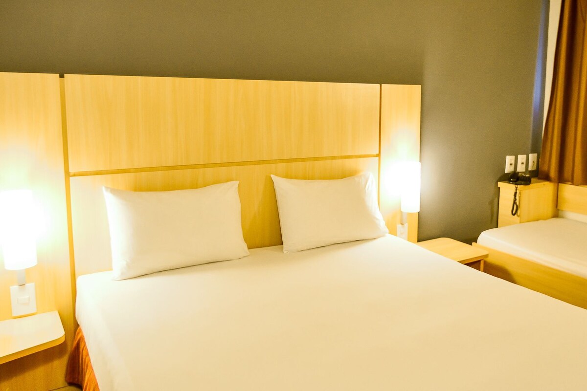 A hotel room with a large bed, two bedside tables, a nightstand, and a lamp.