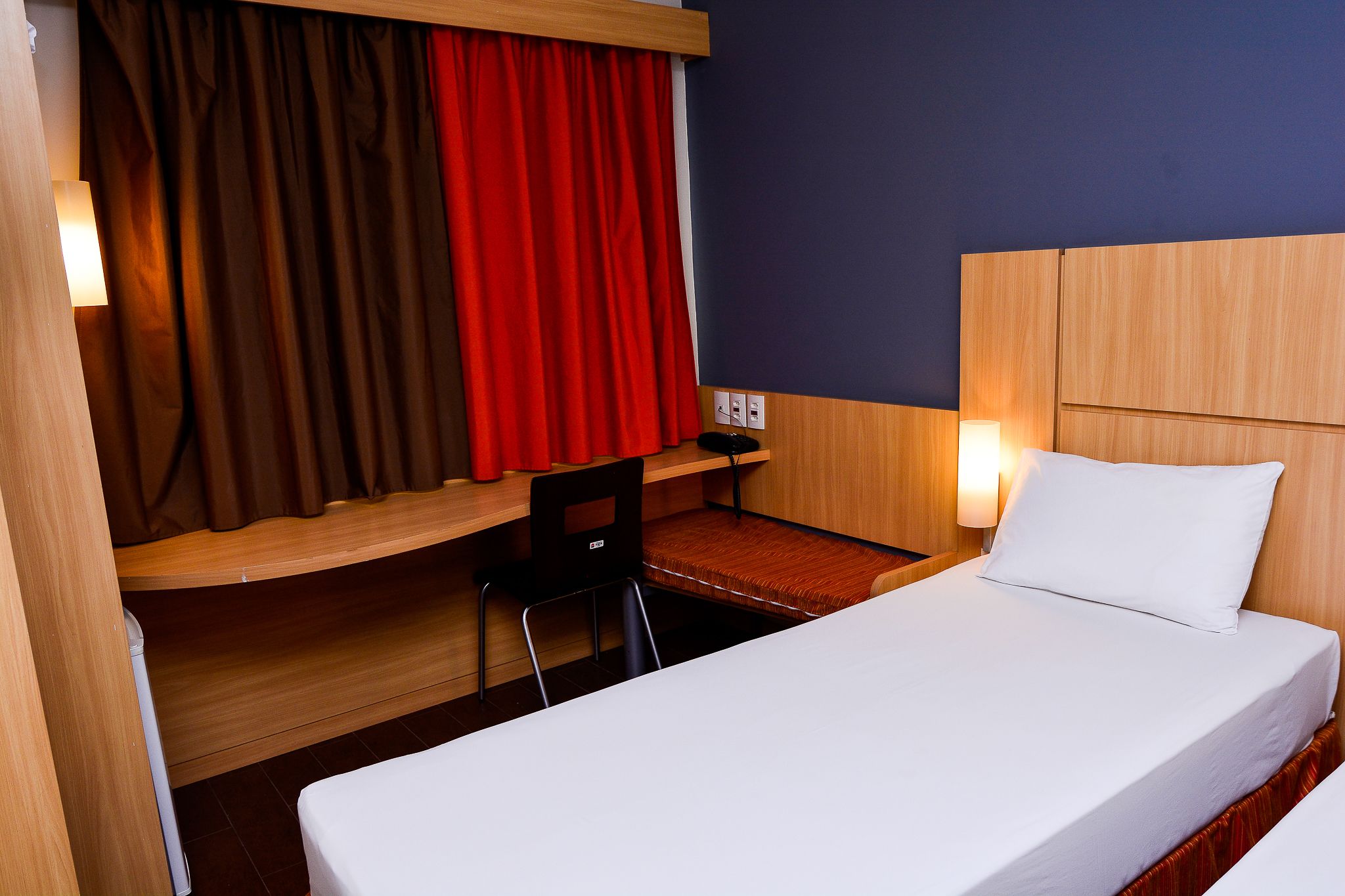 A hotel room with a bed, a desk, a chair, and a window with curtains.