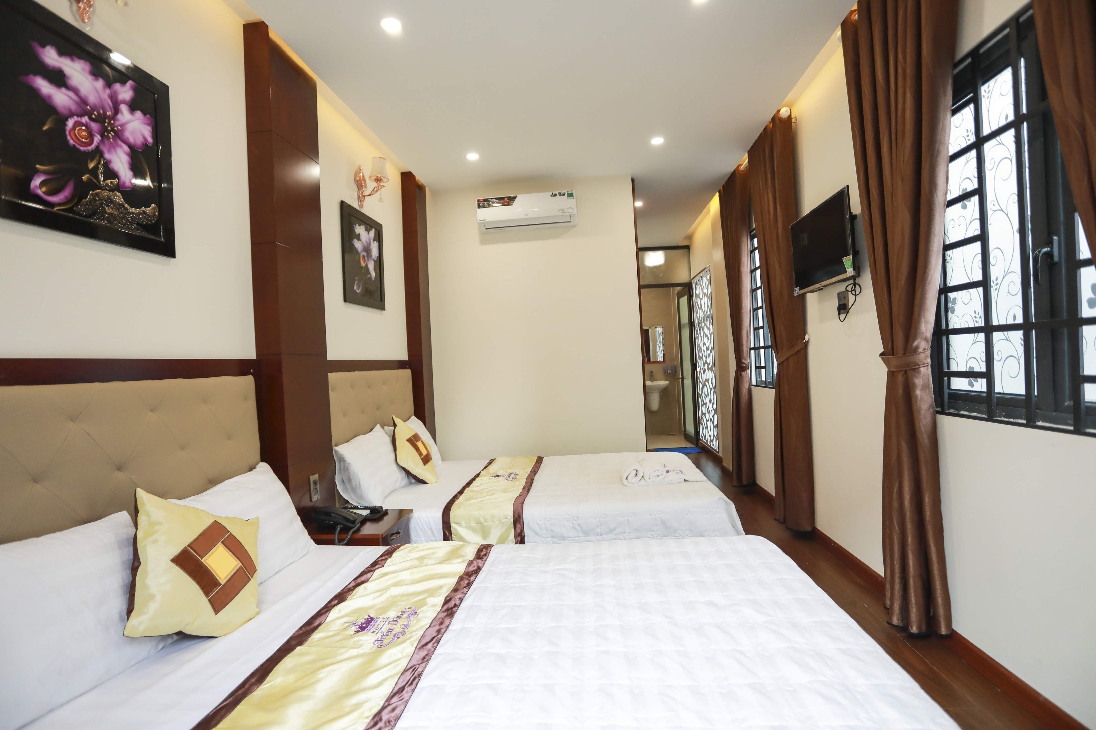 A hotel room with three beds, an air conditioning unit, a television, and a window with curtains.