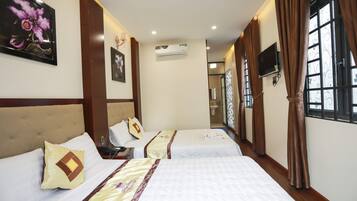 A hotel room with three beds, an air conditioning unit, a television, and a window with curtains.