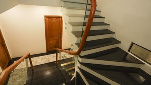 Un escalier avec une main courante en bois et des rampes en verre, menant à une porte portant une plaque avec un numéro.
