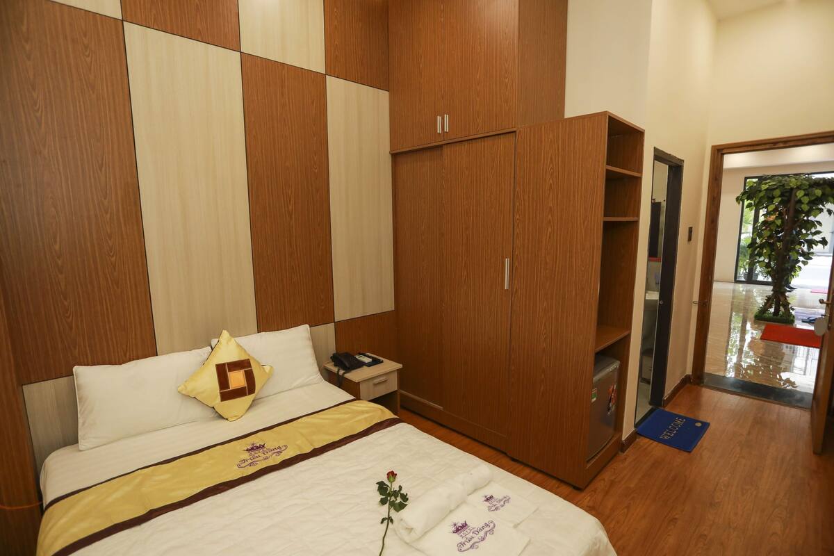 Une chambre d’hôtel comprenant un lit, une armoire, une table de chevet et une porte donnant sur un couloir.