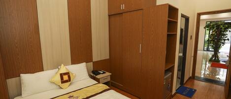 A hotel room with a bed, a wardrobe, a nightstand, and a door leading to a hallway.