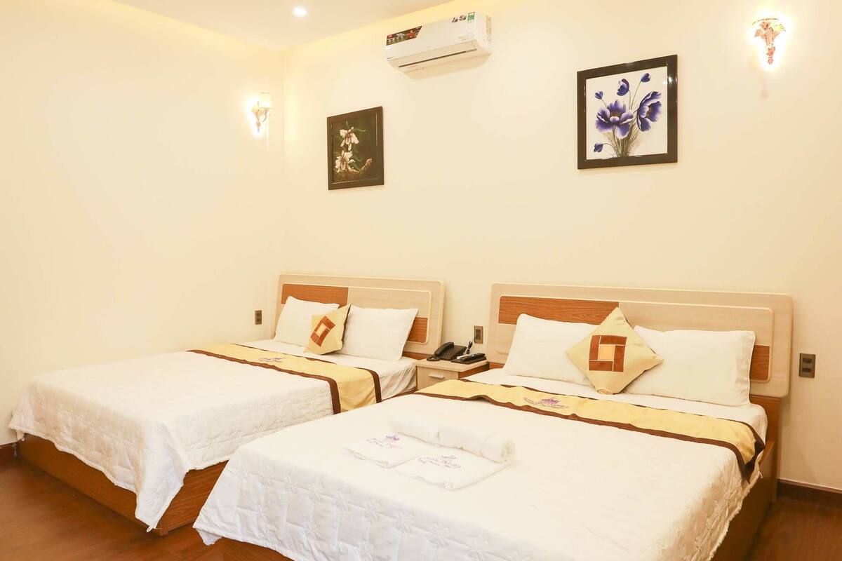 Une chambre d’hôtel avec deux lits simples, un plancher en bois, un climatiseur fixé au plafond et des luminaires fixés au mur.