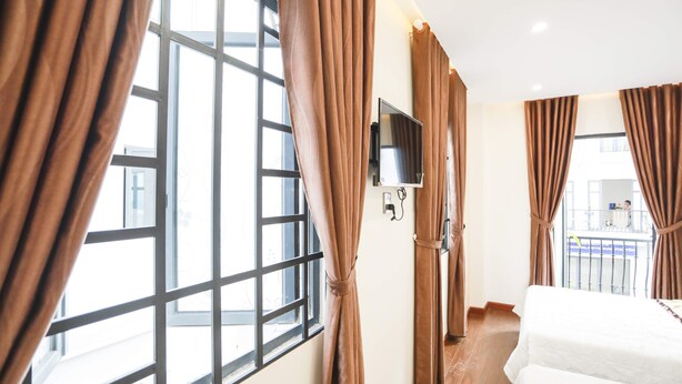 Une chambre d’hôtel dotée de grandes fenêtres, de rideaux, d’un téléviseur à écran plat et d’un lit.
