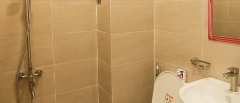 A bathroom with beige tiles, a showerhead, a toilet, and a sink.