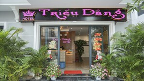 L’extérieur de l’hôtel Trieu Dang, avec son enseigne au néon, ses plantes en pot et un tapis rouge à l’entrée.