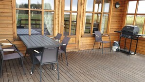 A wooden deck with a table and chairs, a grill, and large windows. - Vorsabær 2 Holiday Home (Selfoss)