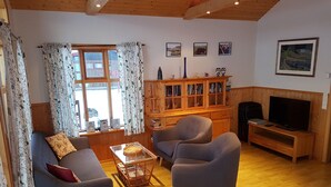 A cozy living room with a sofa, armchairs, a coffee table, and a TV. There's a wooden cabinet with books and decorative items. - Vorsabær 2 Holiday Home (Selfoss)
