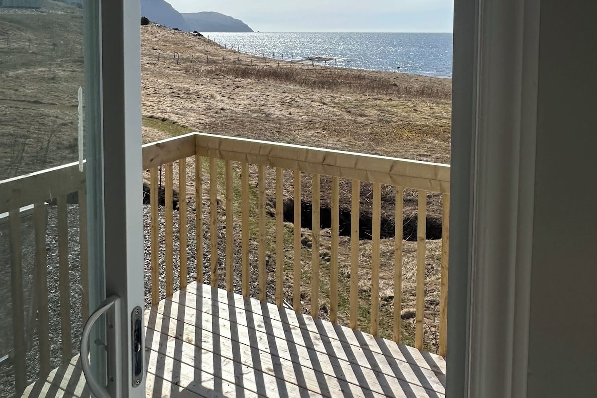 Vista desde un balcón con baranda de madera, sobre una playa con pastizal seco y cielo despejado.