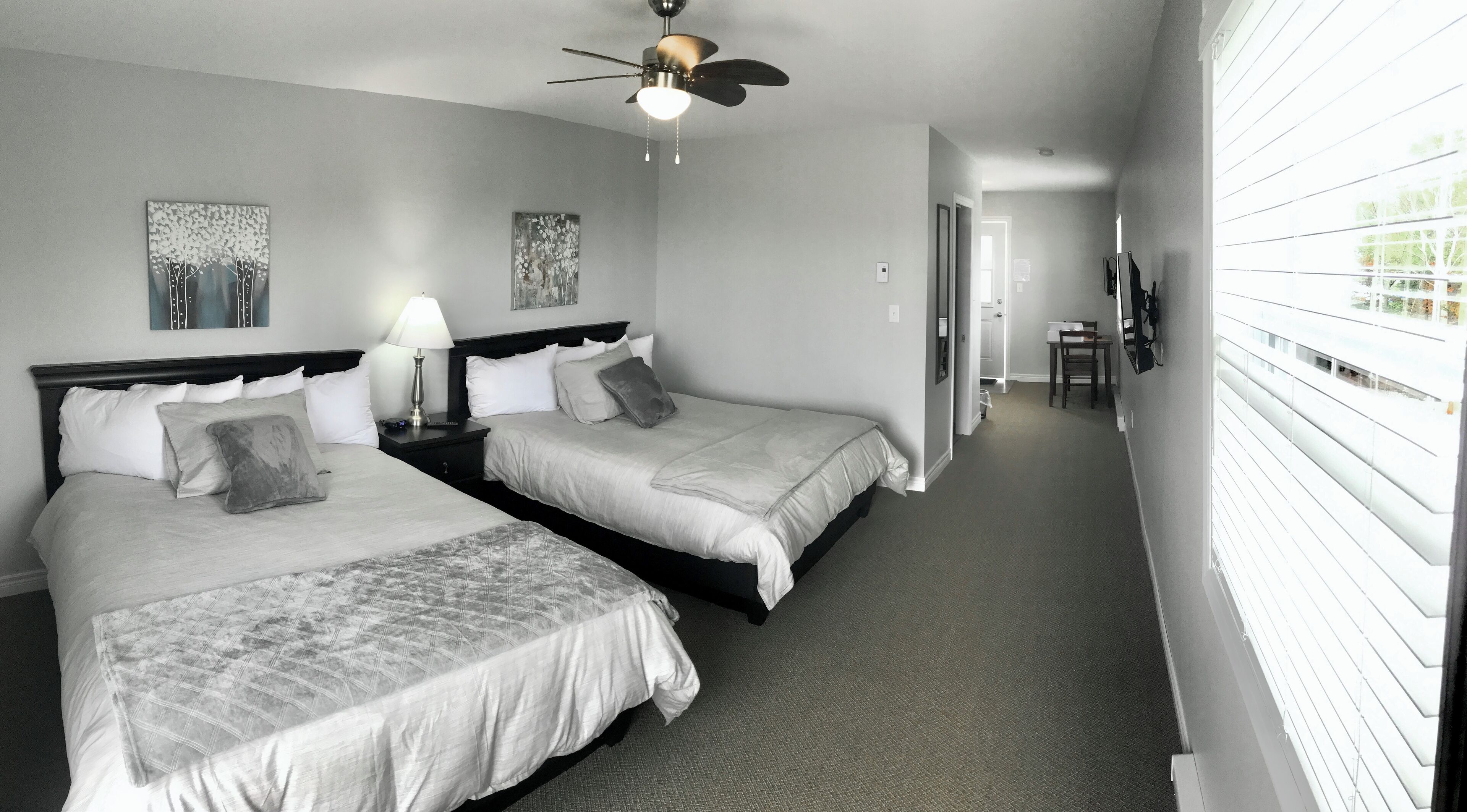 A hotel room with two beds, a ceiling fan, and artwork on the walls.