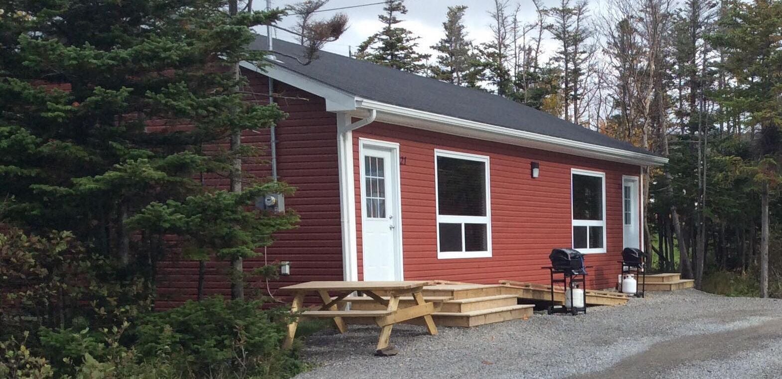 A red cabin with a wooden deck and a picnic table.