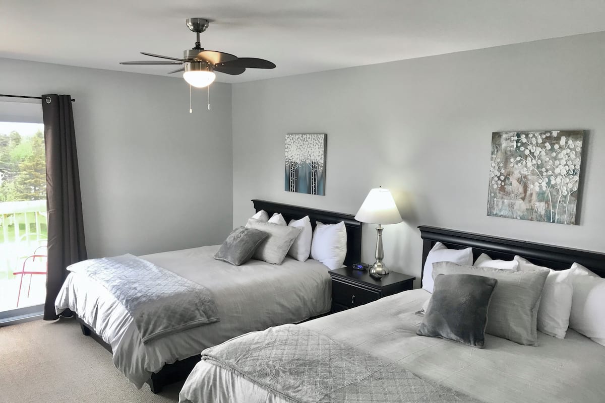 Habitación de hotel con dos camas, un ventilador de techo, una mesita de noche con lámpara y obras de arte en las paredes.