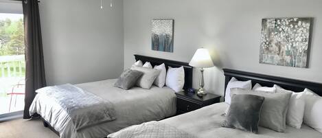 A hotel room with two beds, a ceiling fan, a nightstand with a lamp, and artwork on the walls.