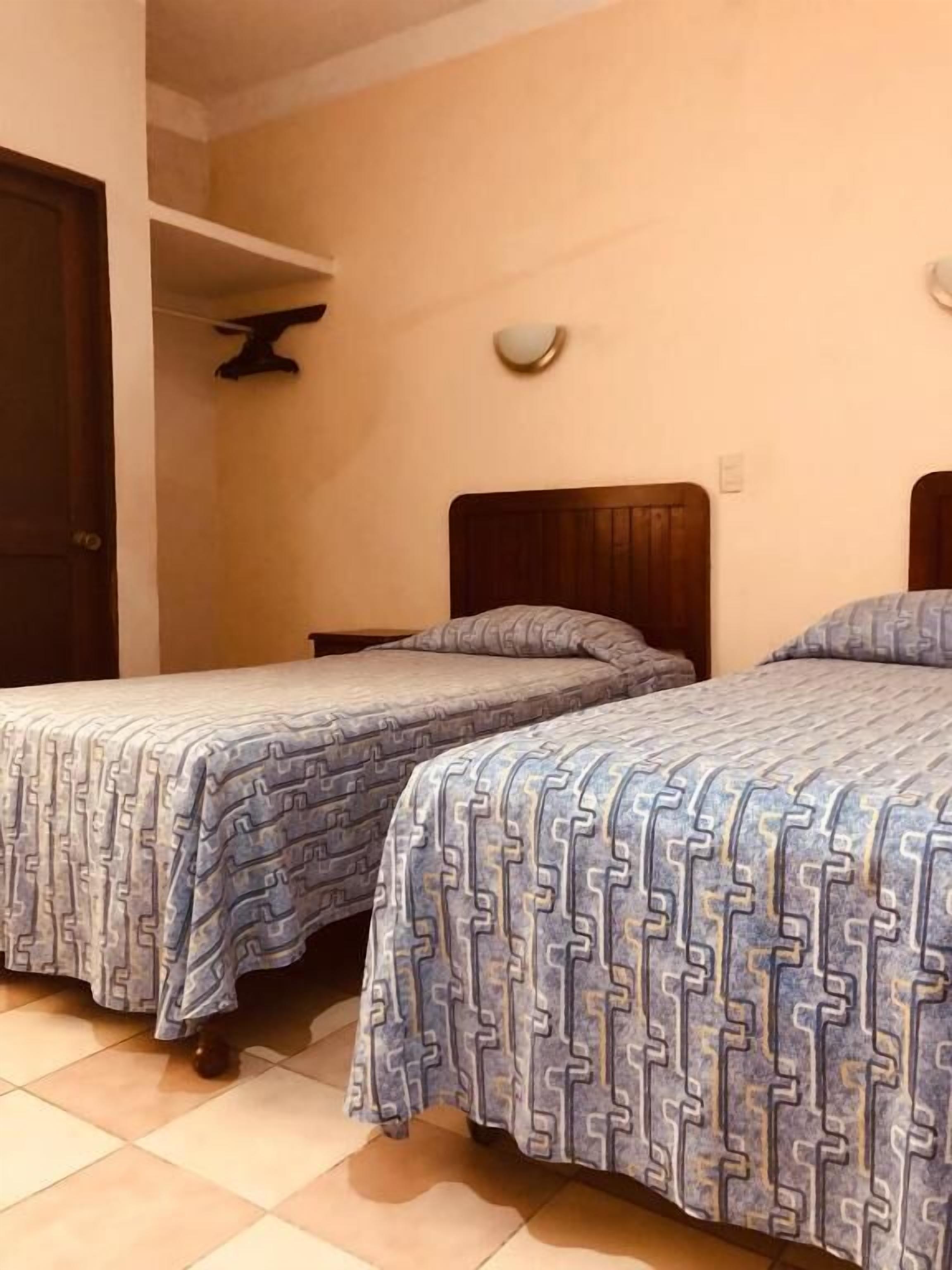 Two single beds with wooden headboards and patterned bedding in a room with tiled flooring.