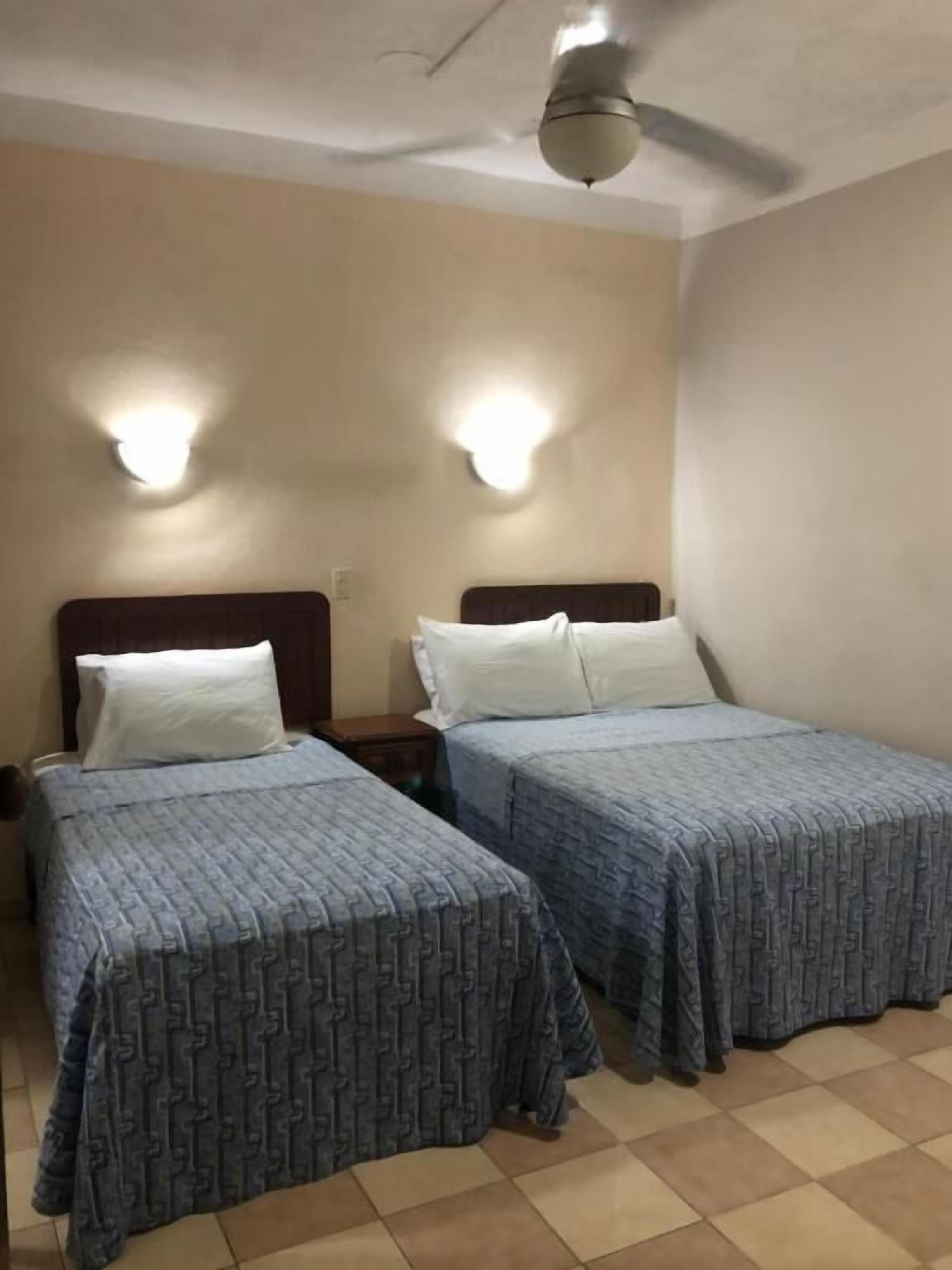 Una habitación de hotel con dos camas individuales, un ventilador de techo e iluminación en la pared.