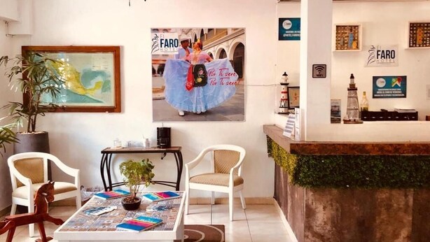 A hotel reception area with a reception desk, chairs, a table with magazines, a potted plant, and a poster on the wall. - Hotel El Faro Veracruz (Veracruz)