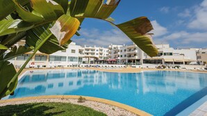 A swimming pool with a clear blue water surface, surrounded by a poolside area with lounge chairs and a building with multiple balconies in the background. - Dunas do Alvor - Torralvor (Portimão)