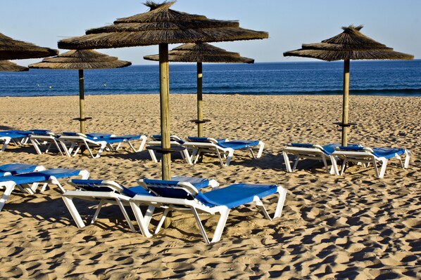 A beach with rows of sun loungers and thatched umbrellas.