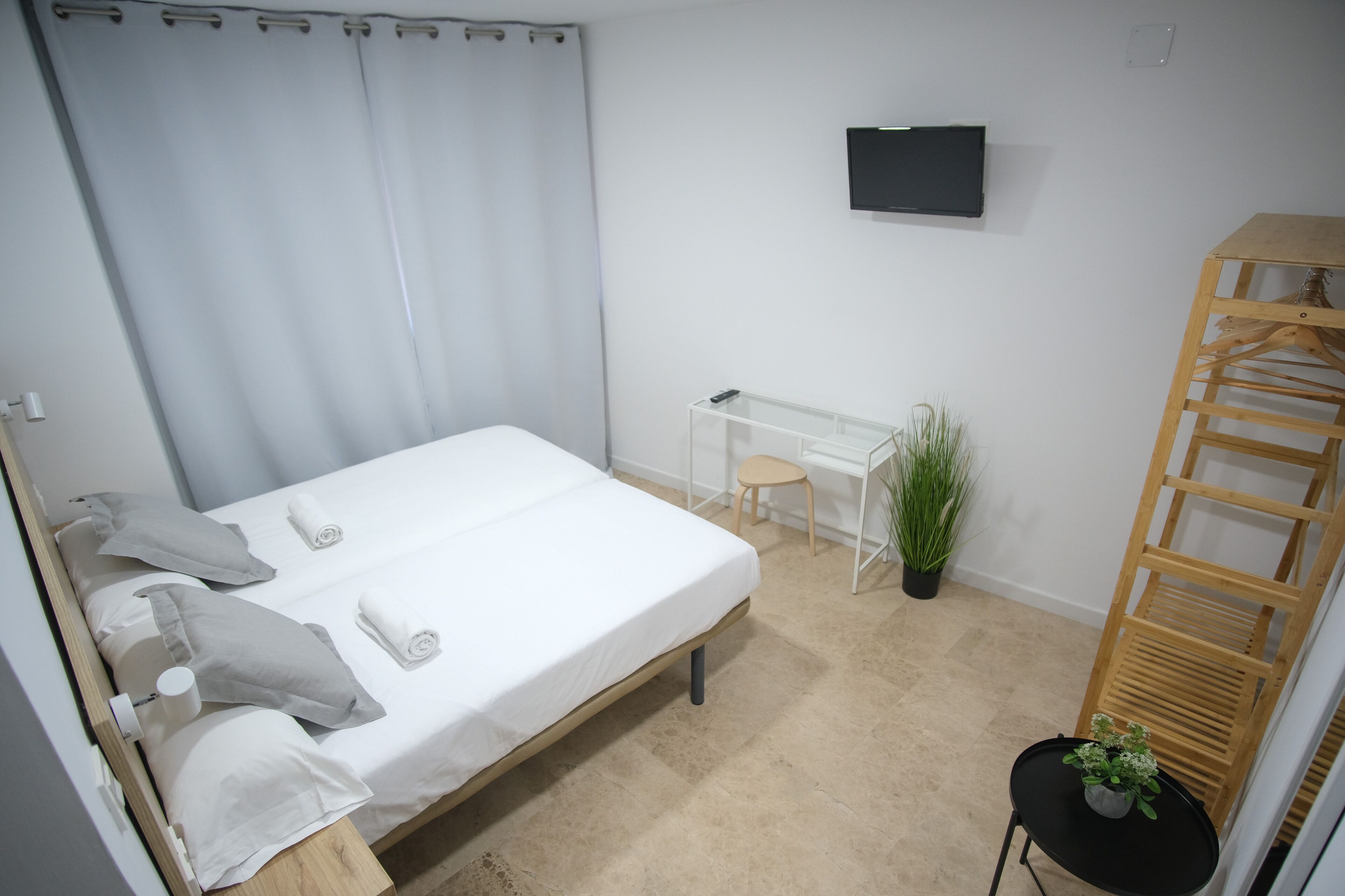 A bedroom with a bed, a desk, a chair, a small table with a plant, and a wooden ladder.