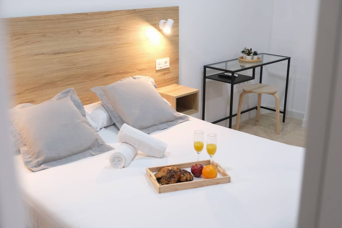 A neatly made bed with pillows, a tray of breakfast including croissants, apples, and oranges, and two glasses of orange juice.