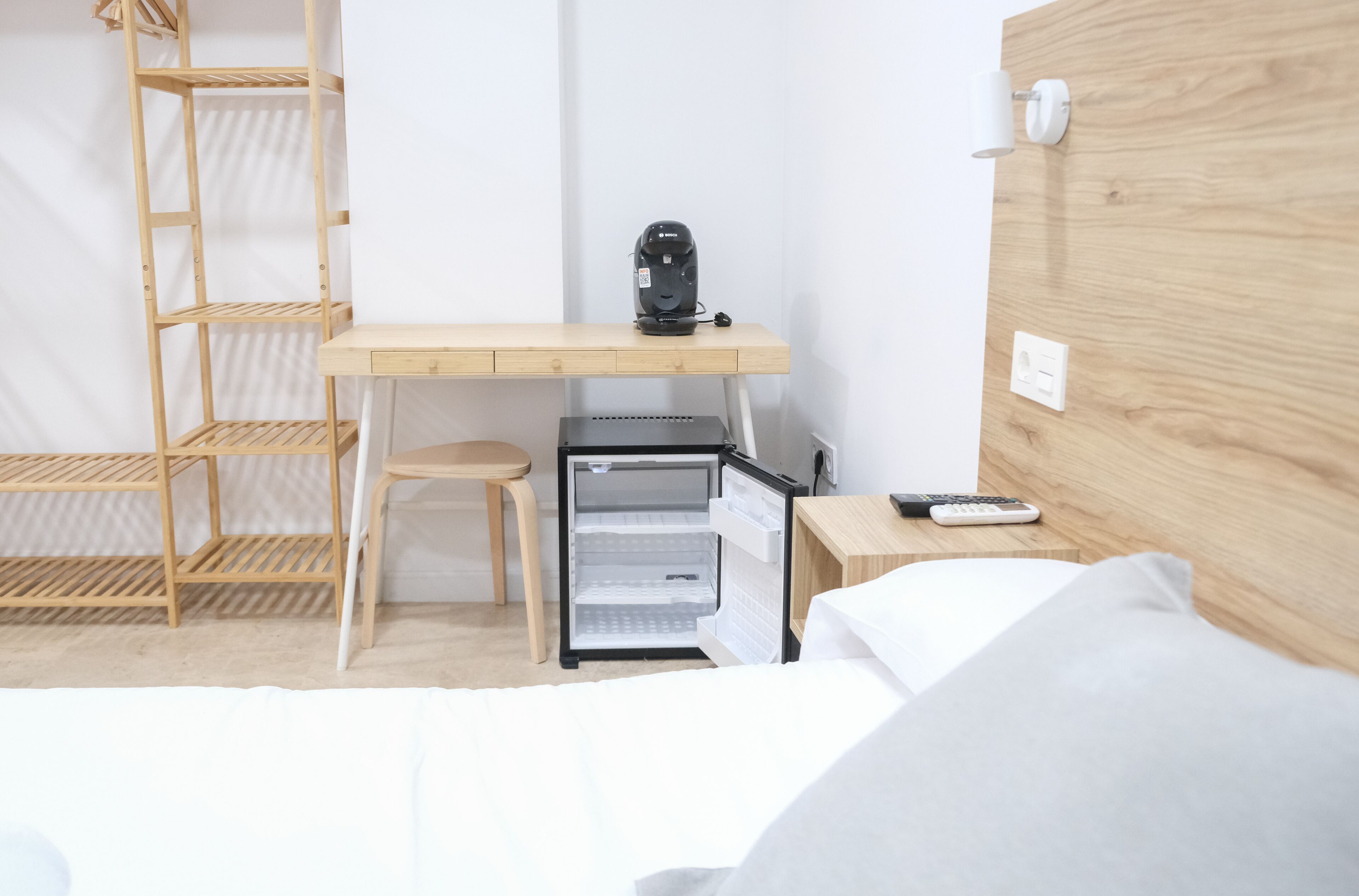 A compact hotel room with a wooden desk, a small refrigerator, a chair, and a bed.