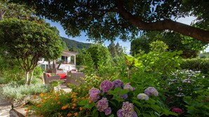 Un jardin avec un espace aménagé pour s’asseoir, un bâtiment doté d’un balcon et une montagne en arrière-plan.