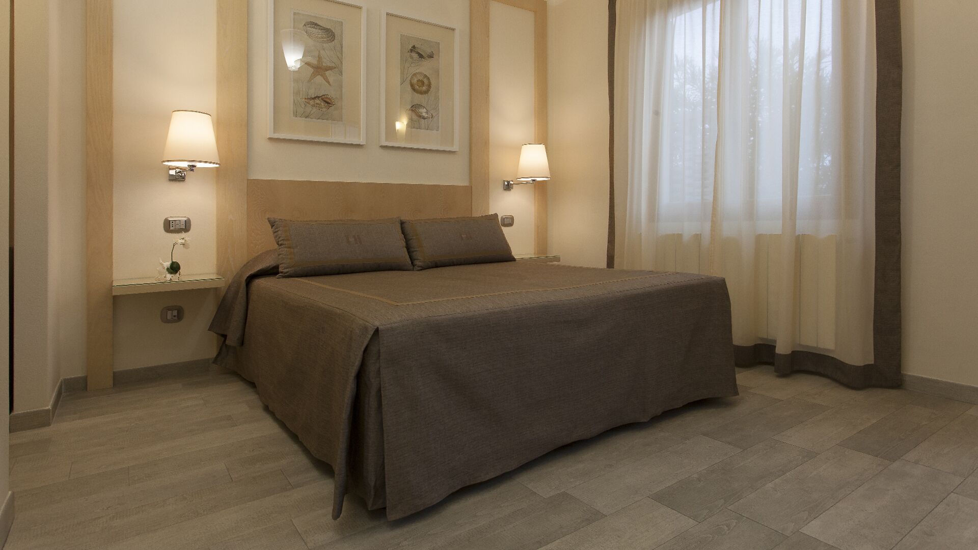 Ein Hotelzimmer mit einem Bett, zwei Nachttischlampen und zwei gerahmten Bildern an der Wand.