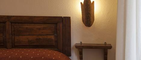 A bedroom with a wooden headboard, a wall-mounted shelf, and a bed with a patterned cover.