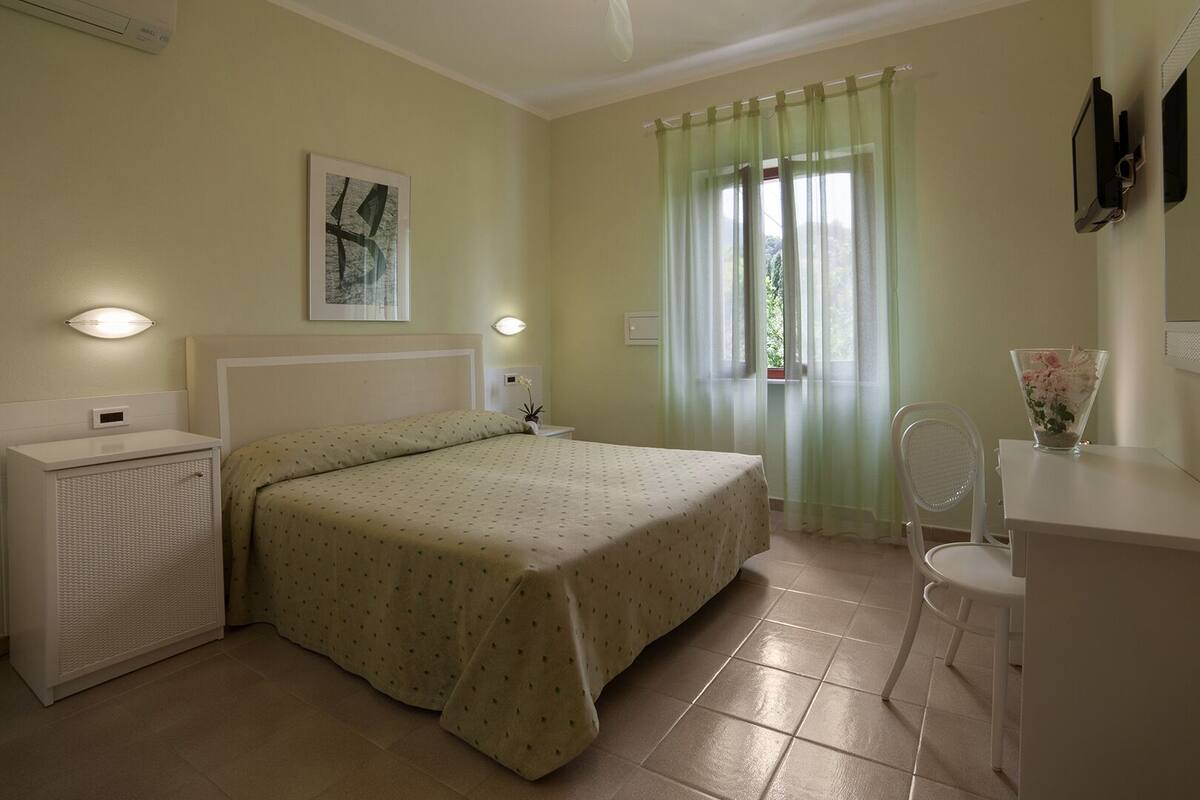 Ein Schlafzimmer mit einem Bett, Nachttischen, einem Schminktisch, einem Spiegel und einem Fenster mit Vorhängen.