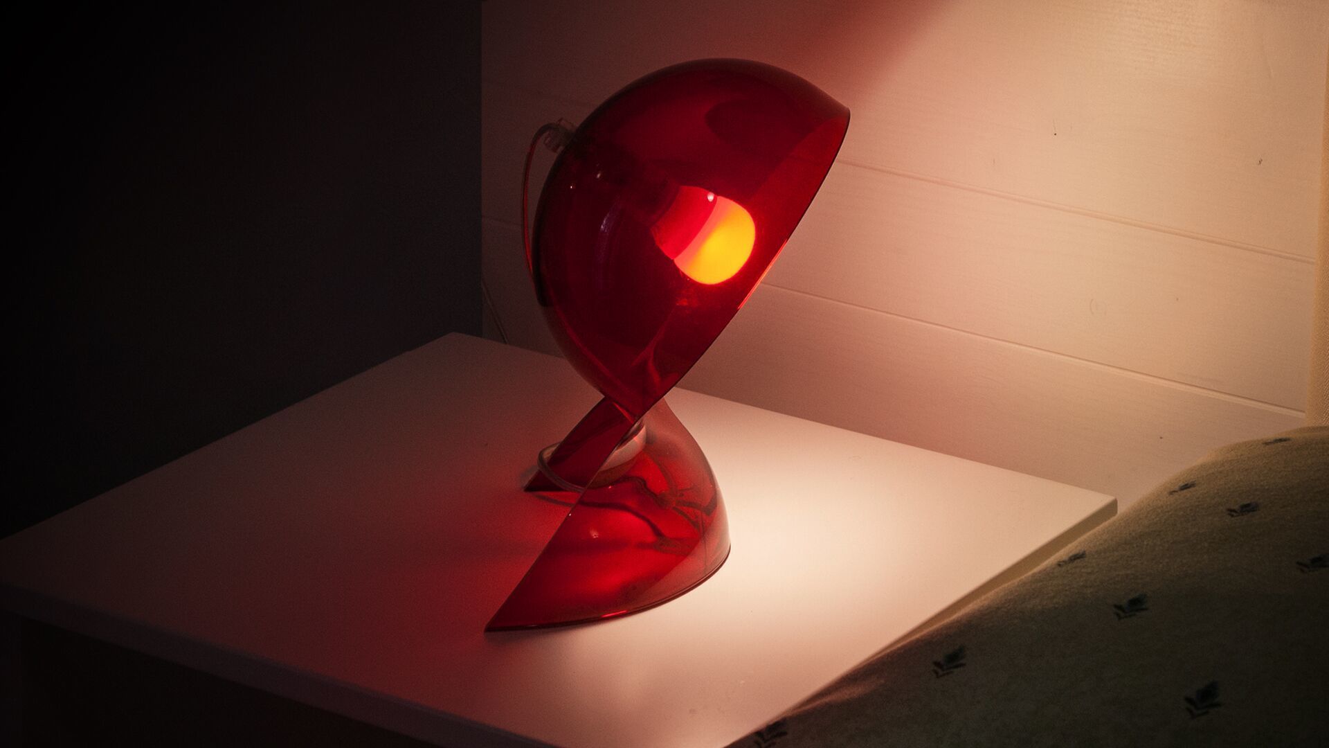A modern red lamp on a white table against a plain wall.