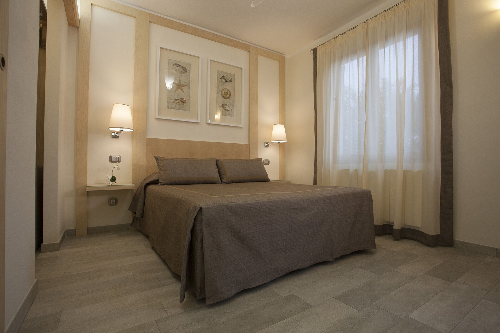 A hotel room with a bed, two bedside lamps, a nightstand, and a window with curtains.