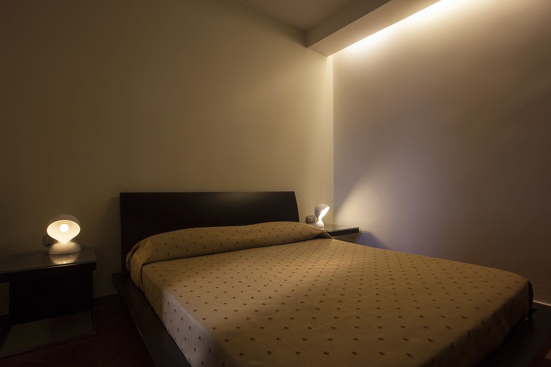 A bedroom with a bed, two bedside tables, and a wall-mounted light fixture.