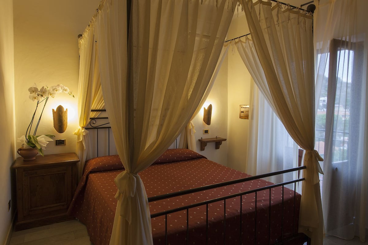 Ein Schlafzimmer mit Bett, Nachttisch, Wandregal und einem Fenster mit Vorhängen.