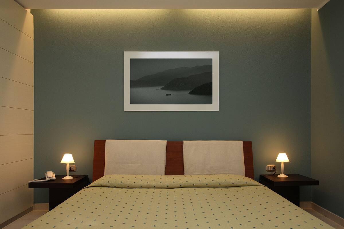 Ein Hotelzimmer mit einem Bett, zwei Nachttischen mit Lampen, einem gerahmten Bild an der Wand und einem Telefon auf einem der Tische.