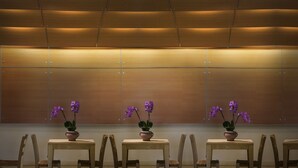 Une pièce aux murs lambrés, avec une table centrale entourée de chaises et des pots d’orchidées violettes.
