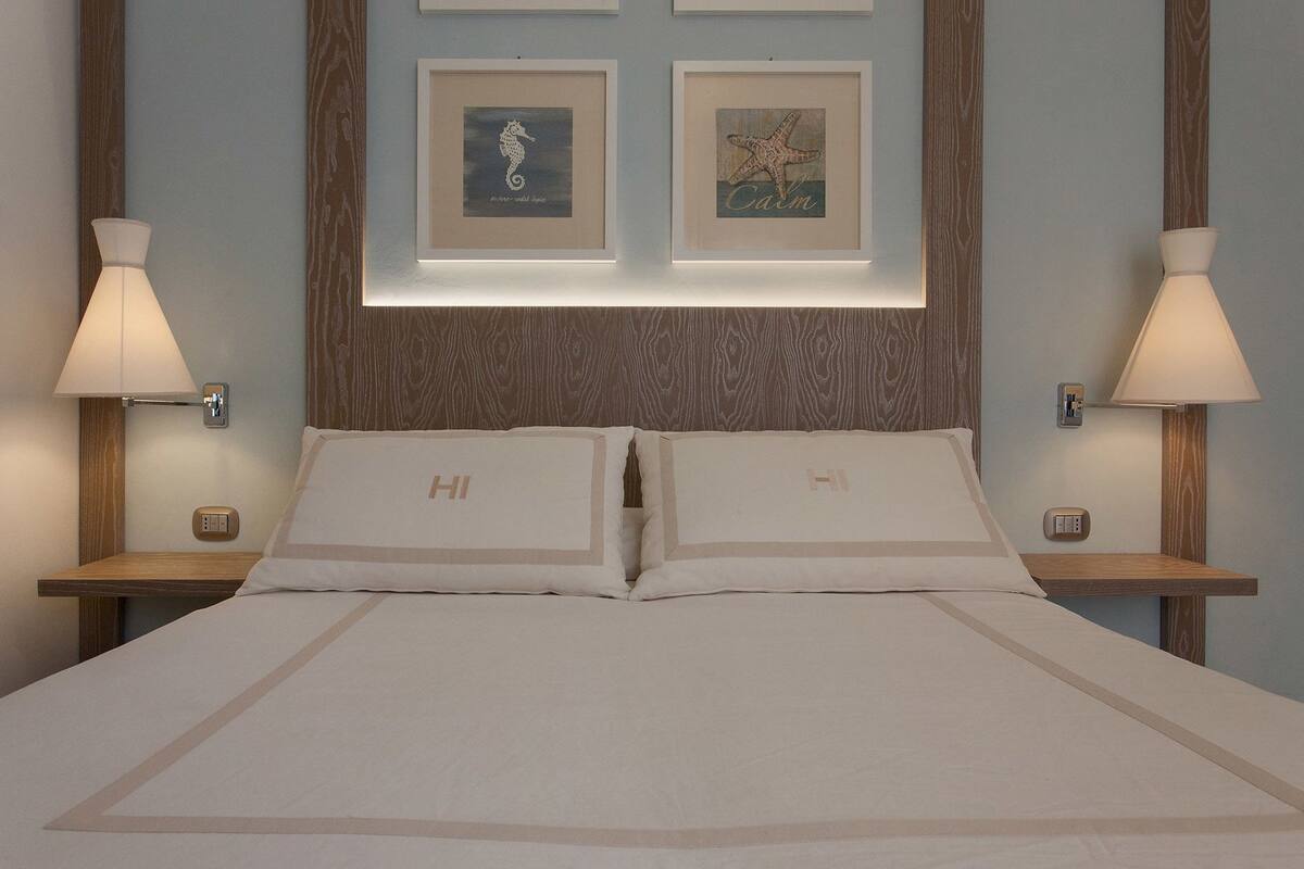 Ein Hotelzimmer mit einem großen Bett, zwei Nachttischen mit Lampen und zwei gerahmten Bildern an der Wand.