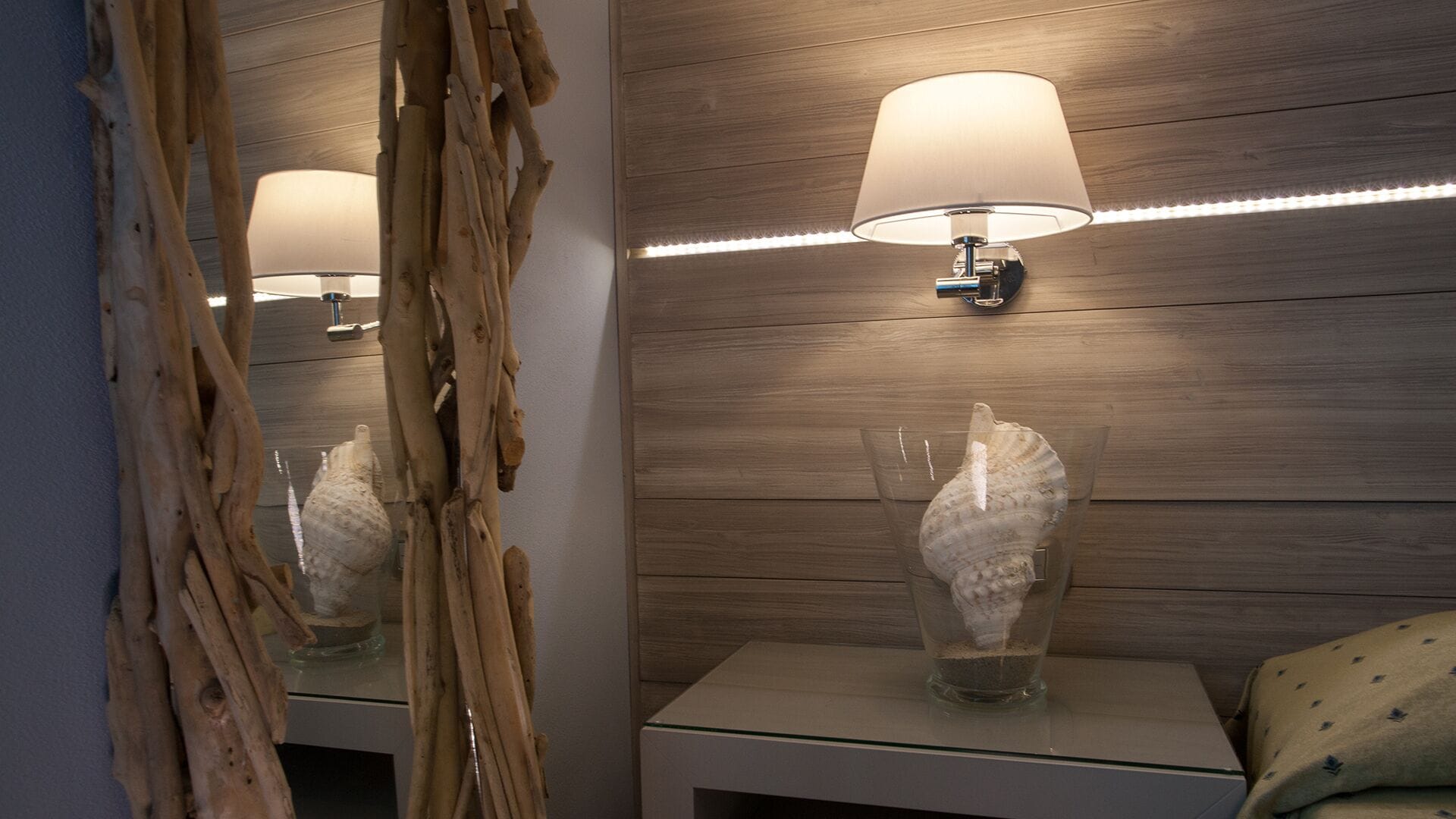 A bathroom with a wooden wall, a mirror, a bedside table, a lamp, and a decorative shell.