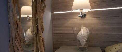 A bathroom with a wooden wall, a mirror, a bedside table, a lamp, and a decorative shell.