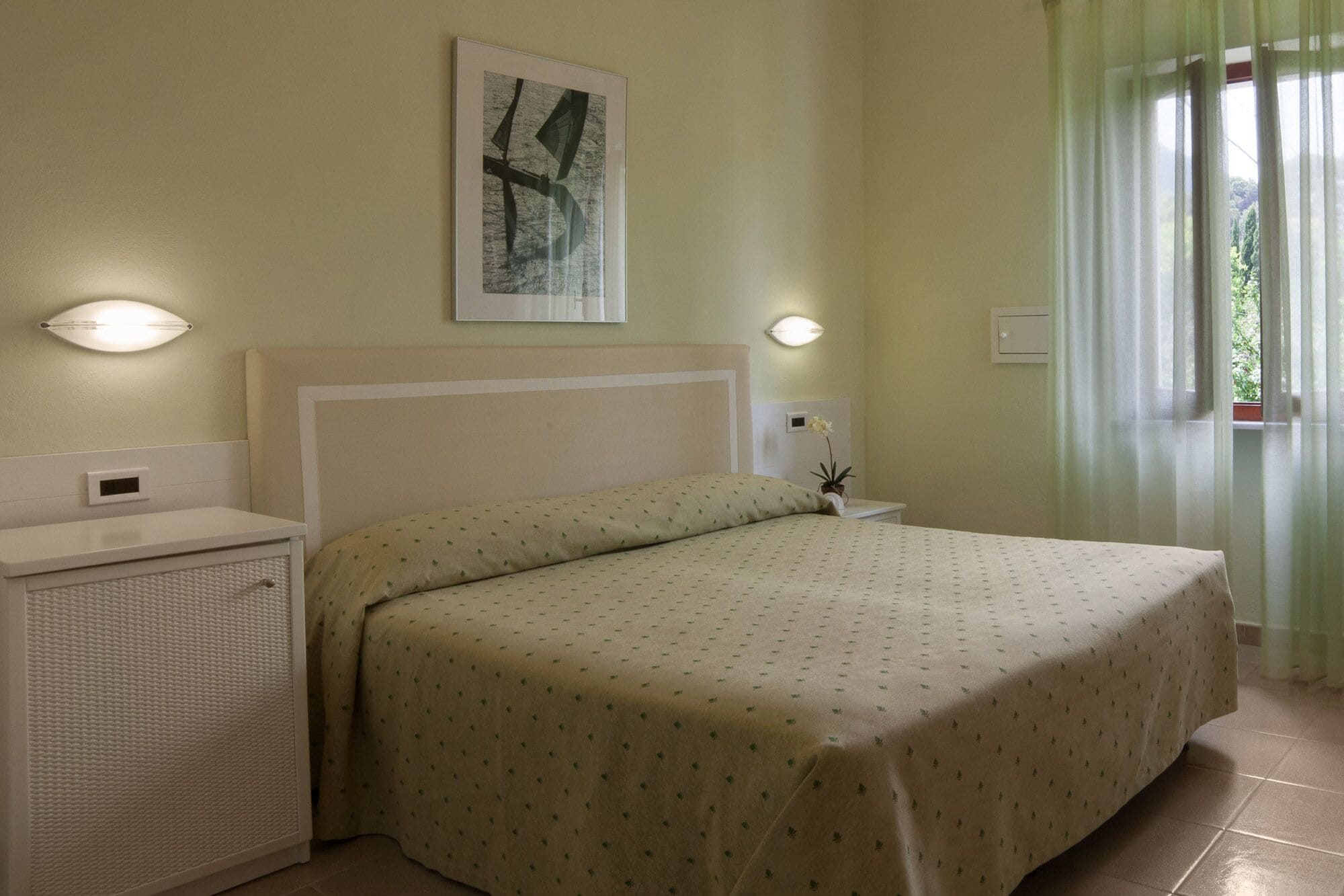 Une chambre à coucher avec un lit, des tables de chevet, un radiateur et une fenêtre avec des rideaux.