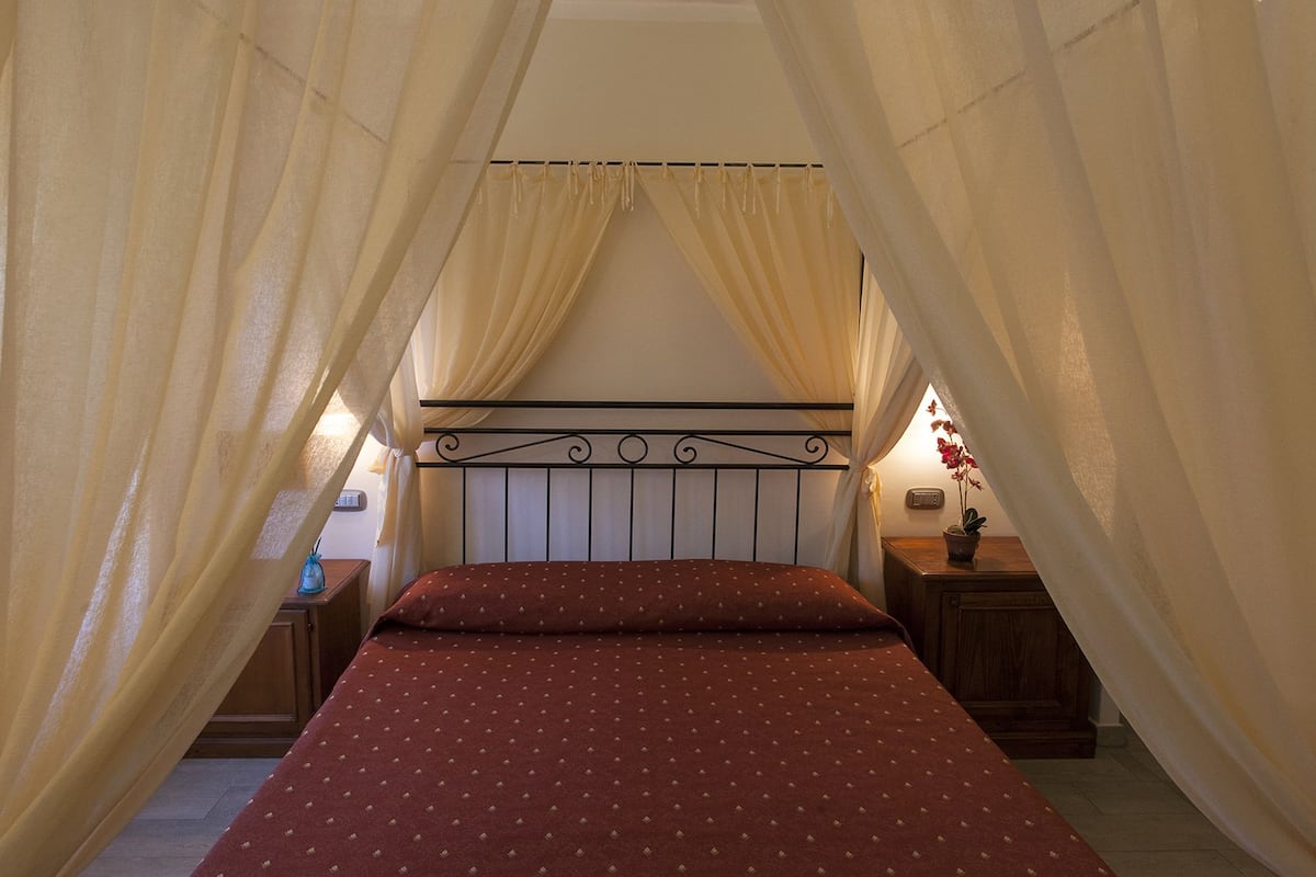 Ein Schlafzimmer mit Bett, Vorhängen, einem Nachttisch und einer Nachttischlampe.