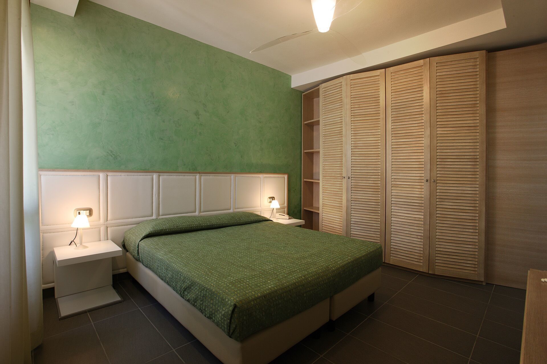A bedroom with a bed, nightstands, a lamp, a wardrobe, and a green wall.