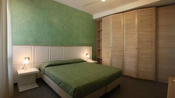 A bedroom with a bed, nightstands, a lamp, a wardrobe, and a green wall.